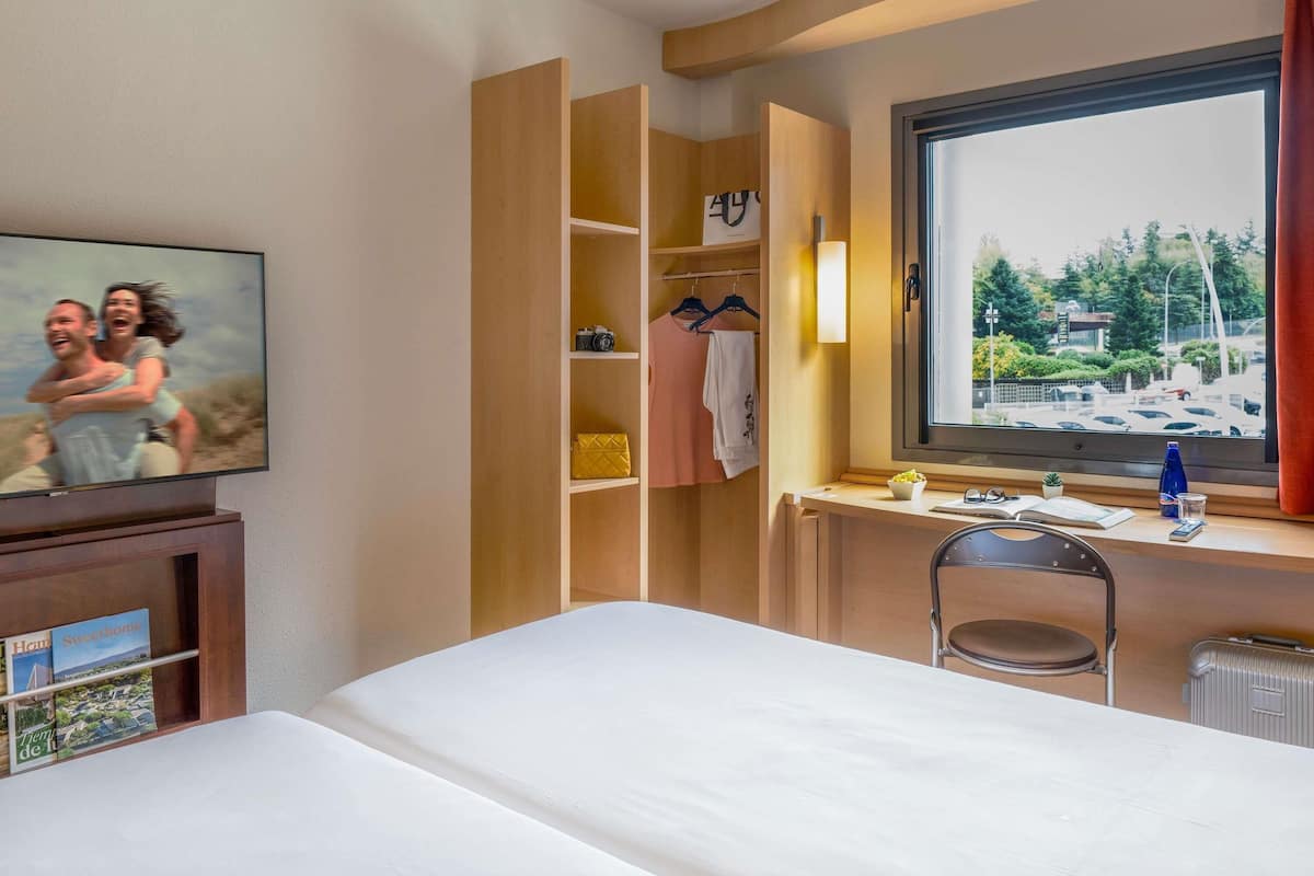 Habitación de hotel con cama, escritorio con silla, armario, televisor y ventana con vistas.