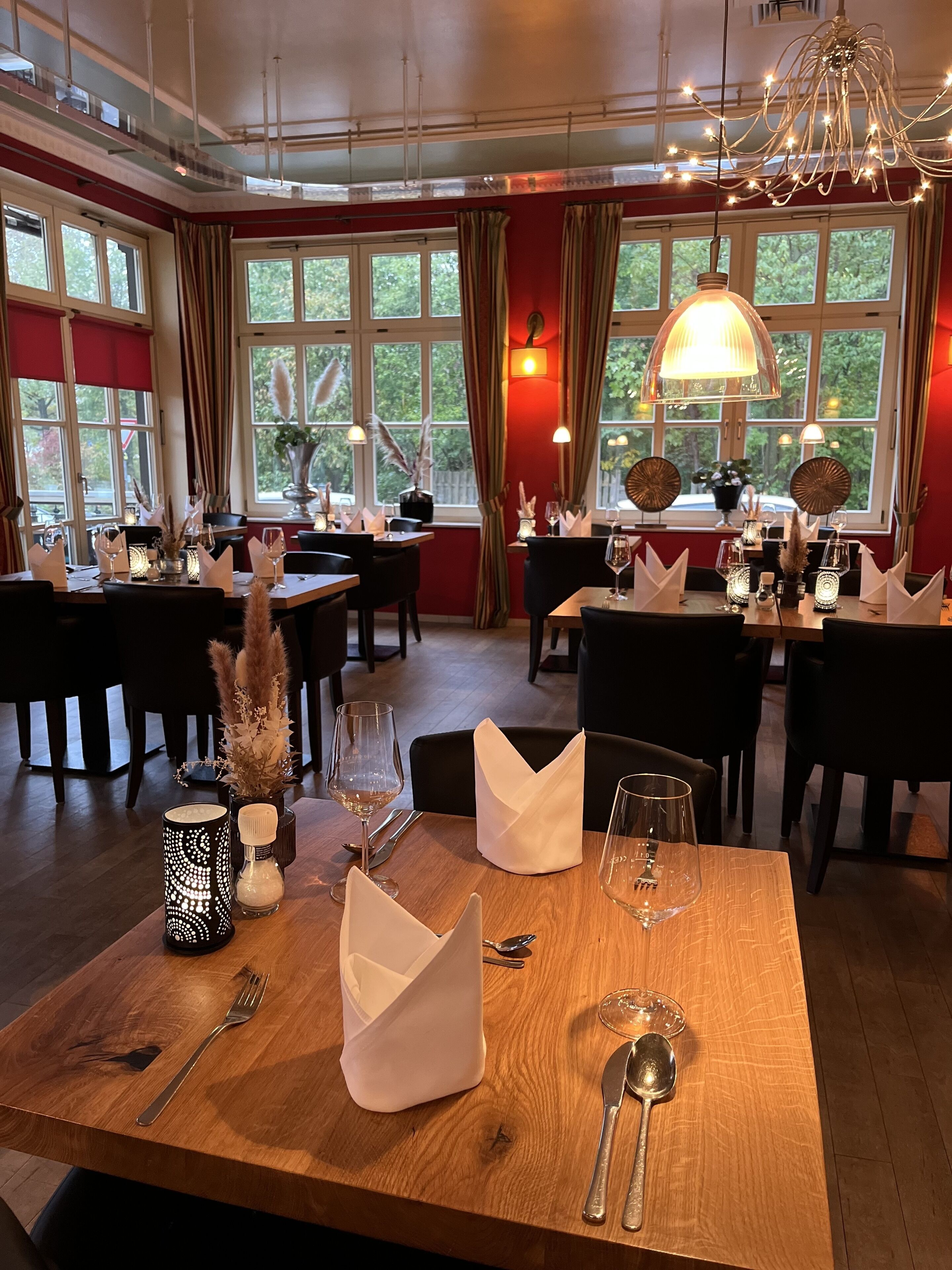 A dining area with tables set for two, featuring candles, napkins, and wine glasses.