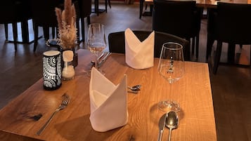 A dining area with tables set for two, featuring candles, napkins, and wine glasses.