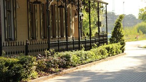 A building with a yellow facade, black iron fence, and a garden with various plants. - Hotel Bentheimer Hof (Bad Bentheim)