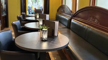 Ein Restaurantinnenraum mit runden Tischen, schwarzen Ledersitzgruppen und einem Buntglasfenster im Hintergrund.