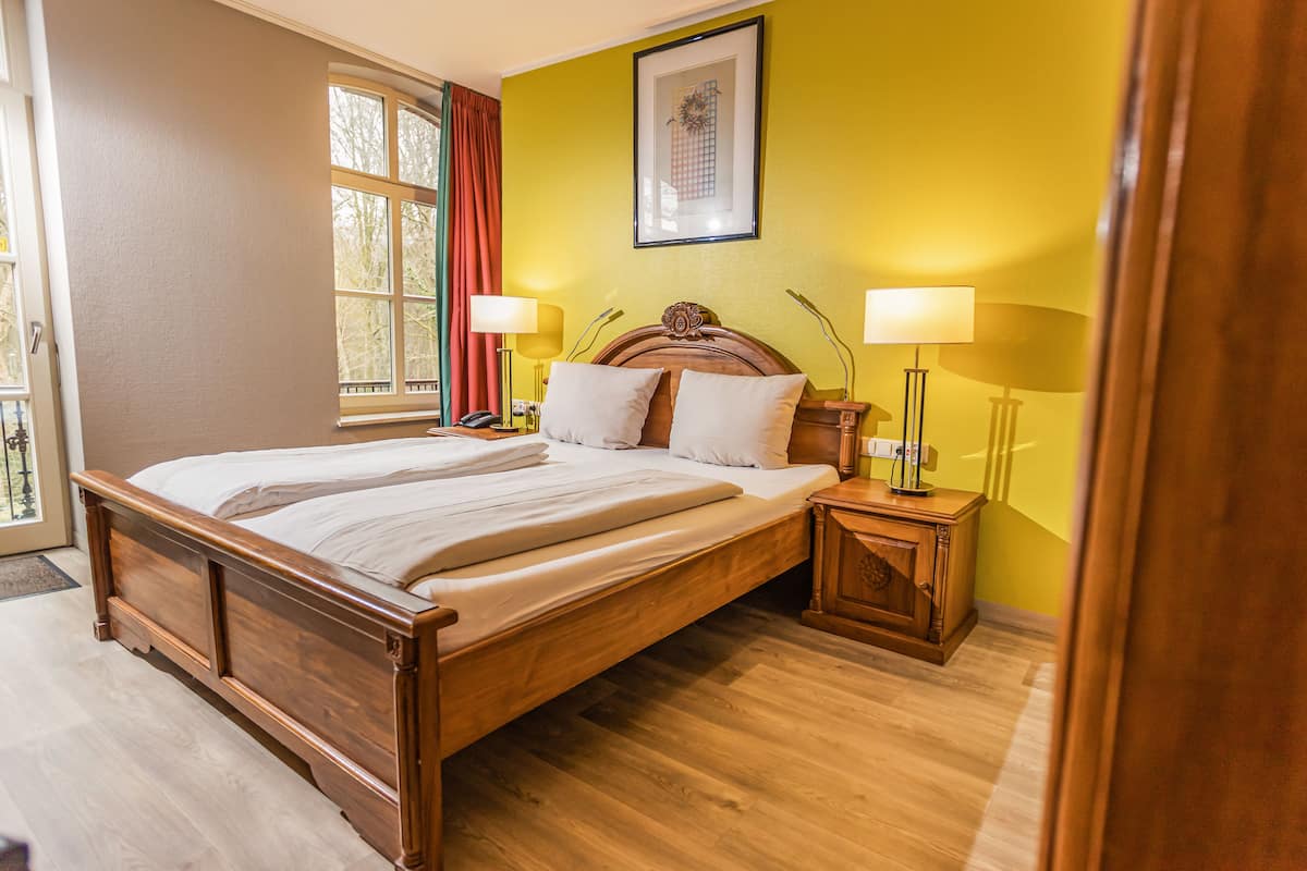 Un lit bien fait, avec du linge de lit blanc, une tête de lit en bois et deux lampes de chevet.