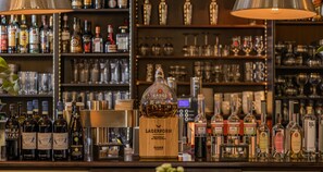 Un espace bar avec différentes bouteilles d’alcool, un comptoir en bois et, au fond, des étagères remplies de verres et de bouteilles.