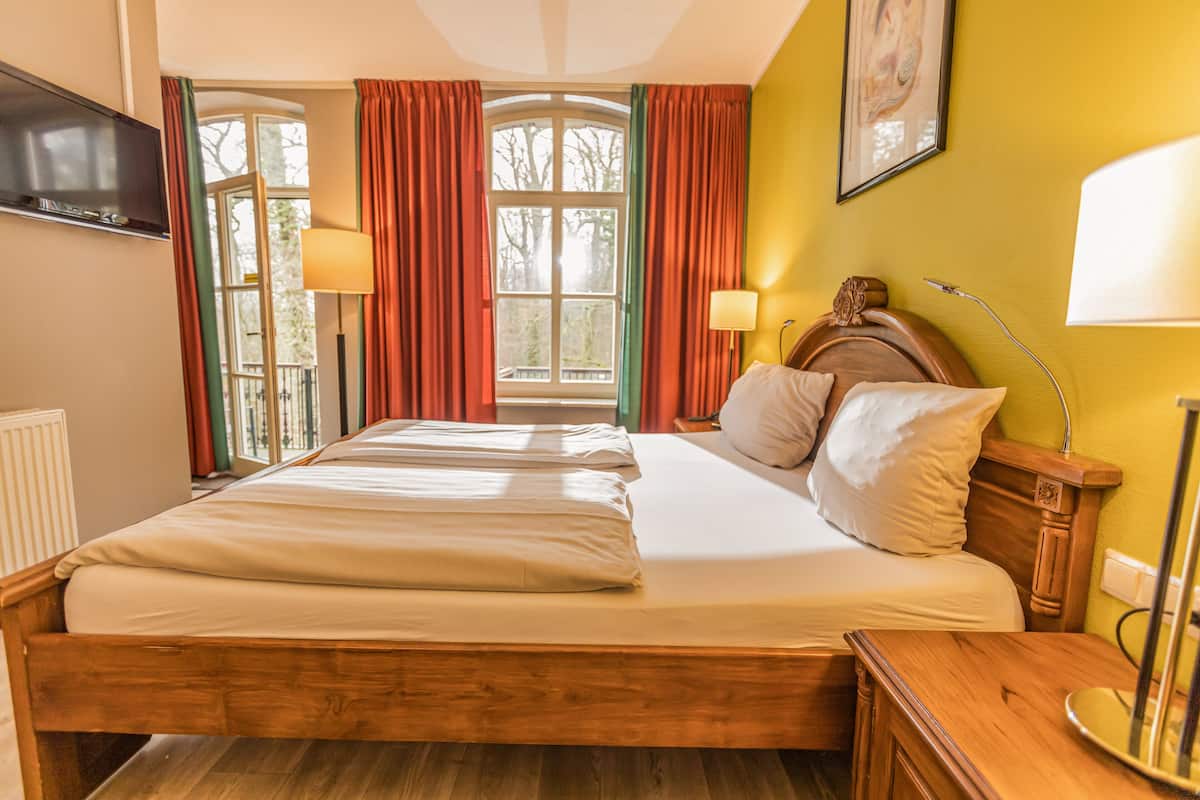 Une chambre d’hôtel avec un grand lit, deux lampes de chevet, une tête de lit en bois et un téléviseur fixé au mur.