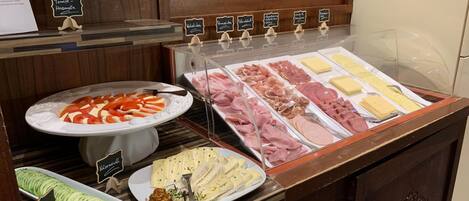 A buffet with various food options including sliced tomatoes, meats, cheeses, and a cucumber dish.