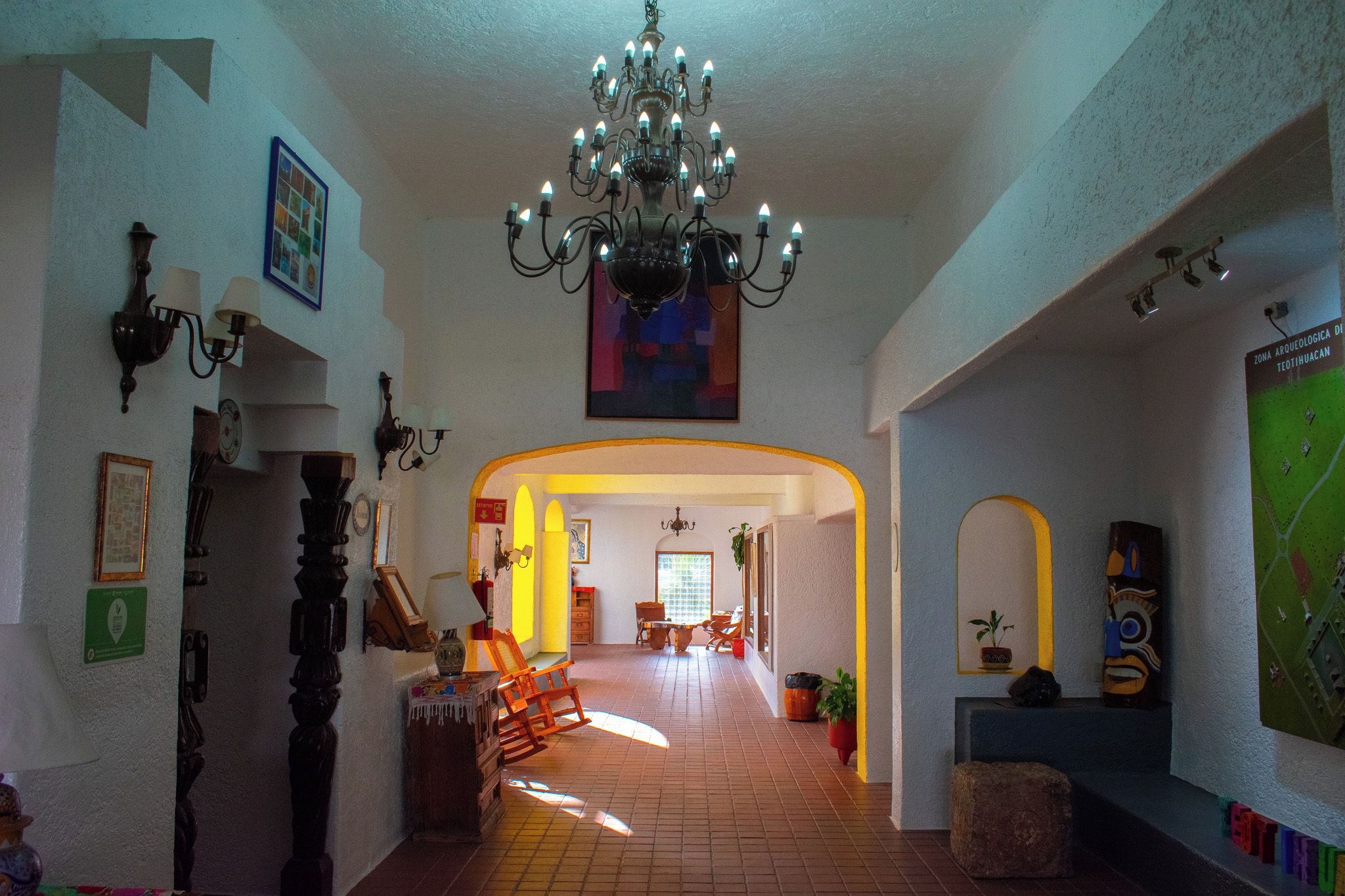 A spacious hallway with a chandelier, framed pictures, and a map on the wall.