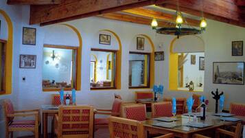 A restaurant interior with wooden beams, arched windows, and framed pictures on the walls.