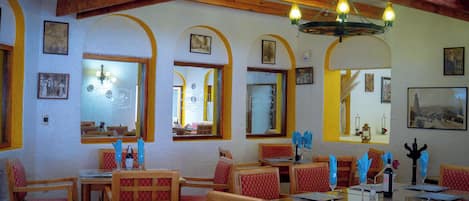 Un interior de restaurante con vigas de madera, ventanas arqueadas y cuadros en las paredes.