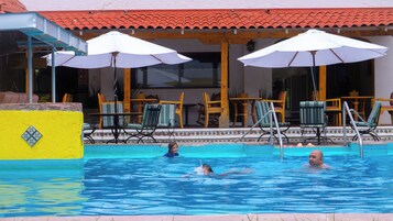 A swimming pool with lounge chairs and umbrellas, a tiled roof, and a yellow wall with a decorative tile.