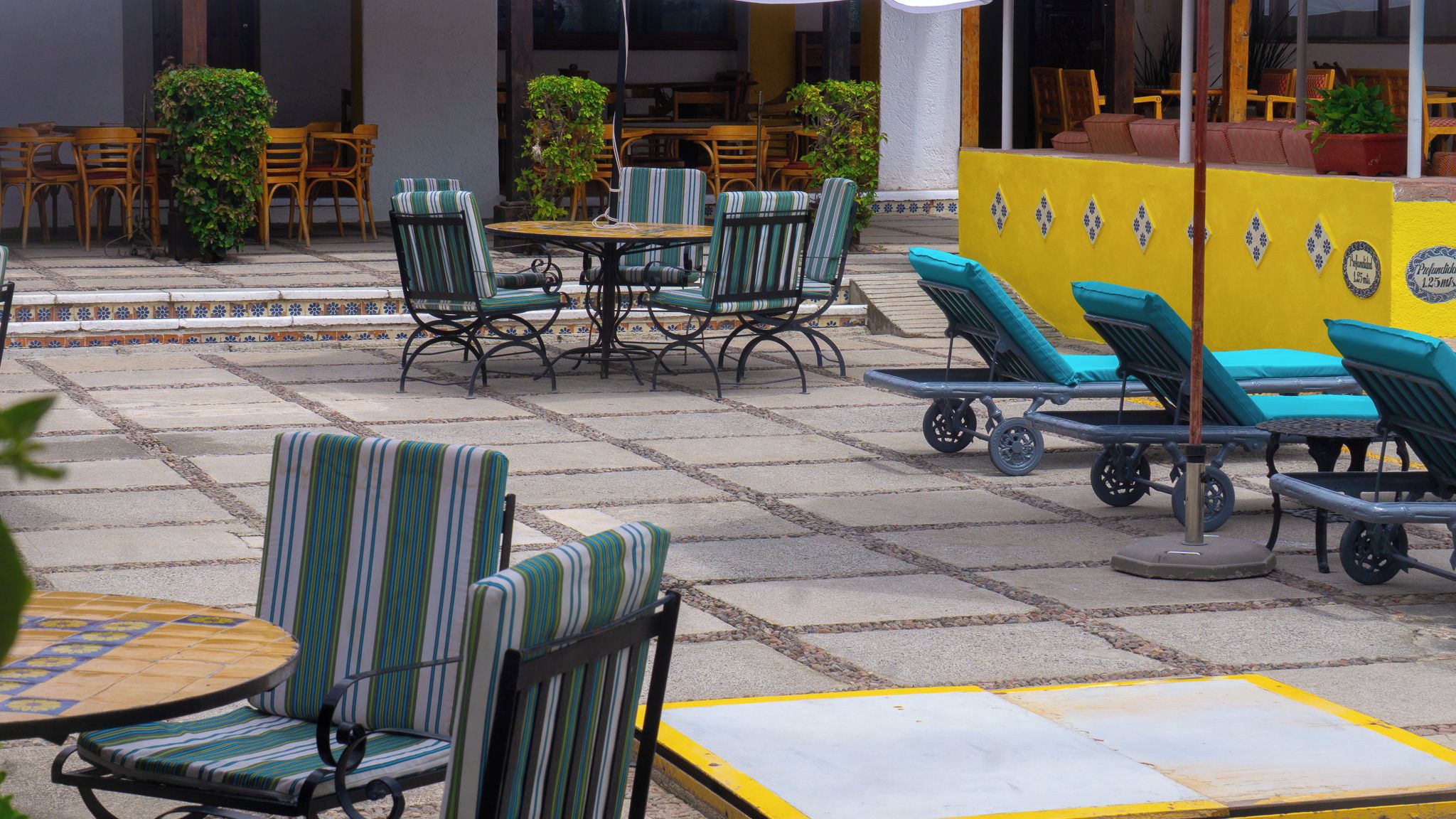 Outdoor seating with striped chairs and tables, a yellow wall with decorative tiles, and a tiled floor.