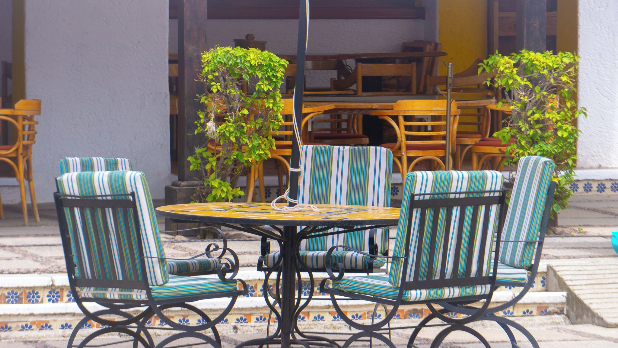 A round table with four striped chairs, a potted plant, and a wooden bench in a courtyard.