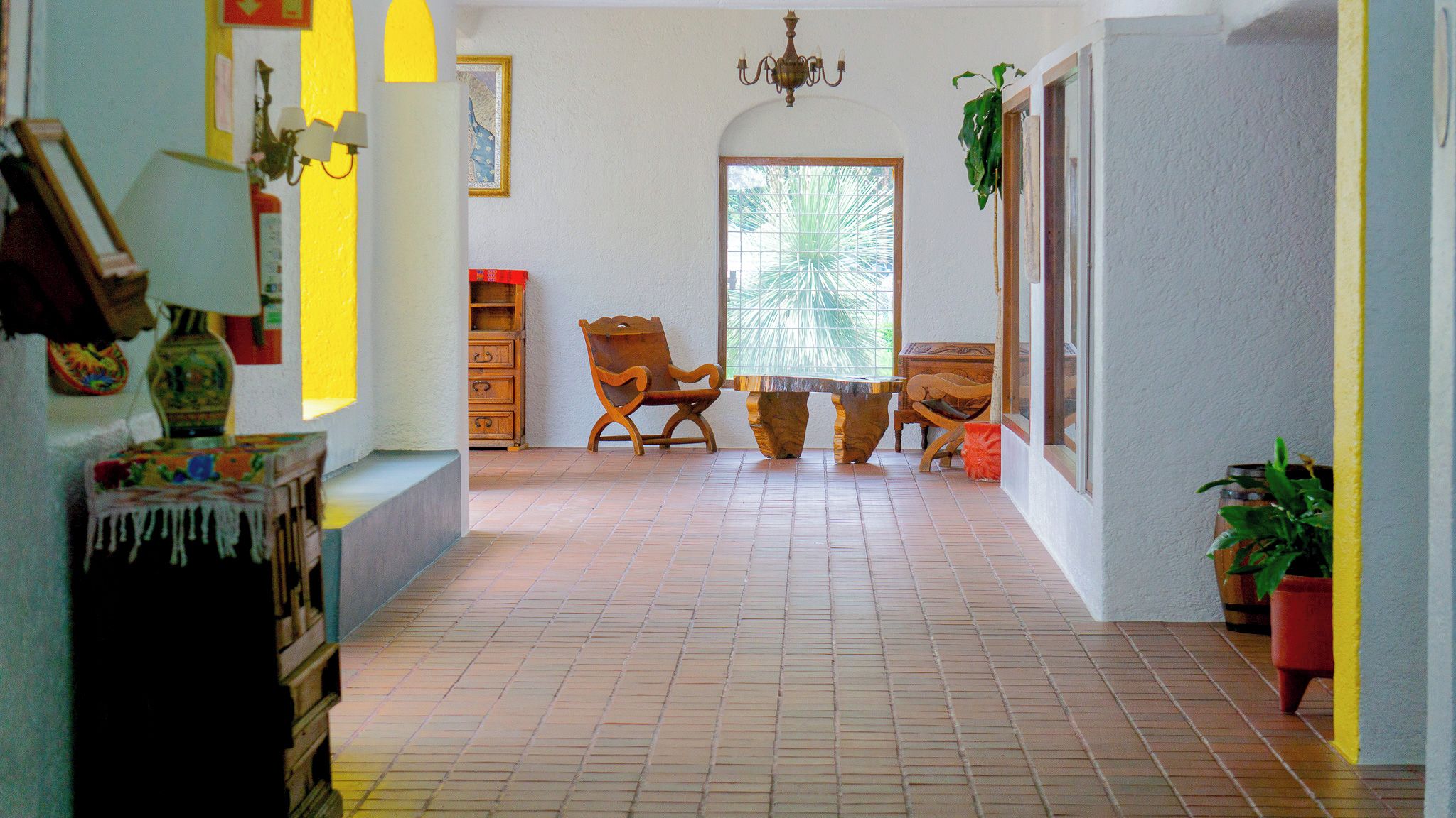 Un pasillo con suelo de baldosas, muebles de madera, un candelabro y una puerta que da al exterior.