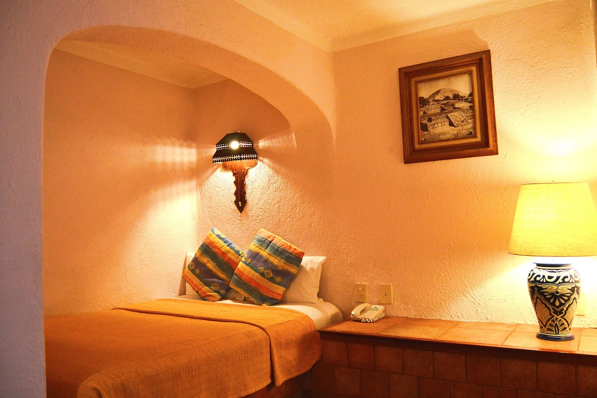 A hotel room with a bed, a nightstand with a lamp, a telephone, and a framed picture on the wall.