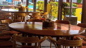 A restaurant with round tables and wooden chairs, a coffee pot on one table, and a yellow wall in the background. - Villas Arqueologicas Teotihuacan (Teotihuacan)