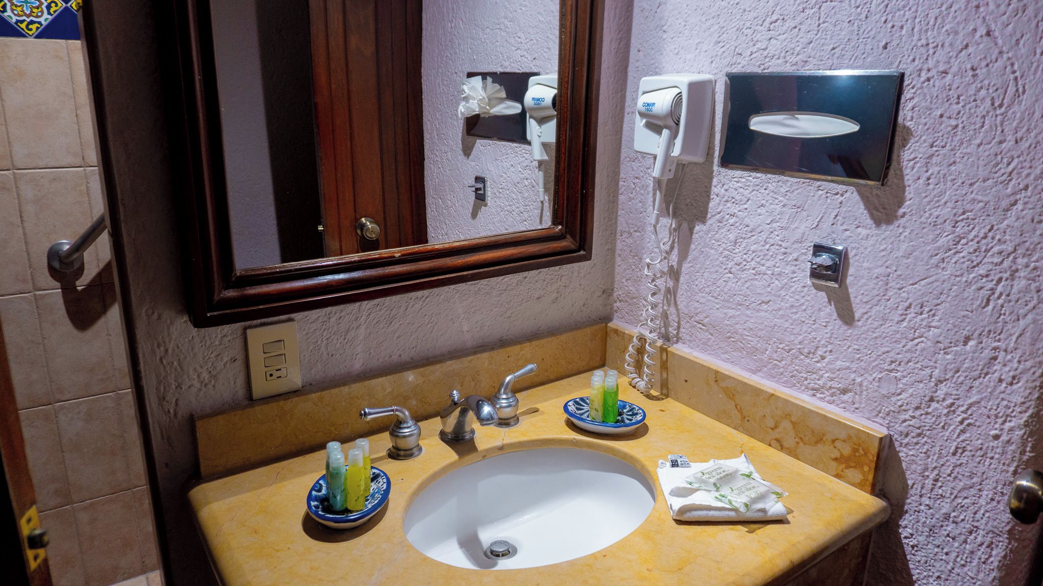 Une salle de bain équipée d’un lavabo, d’un miroir, d’un distributeur de serviettes et d’un distributeur de savon fixé au mur.