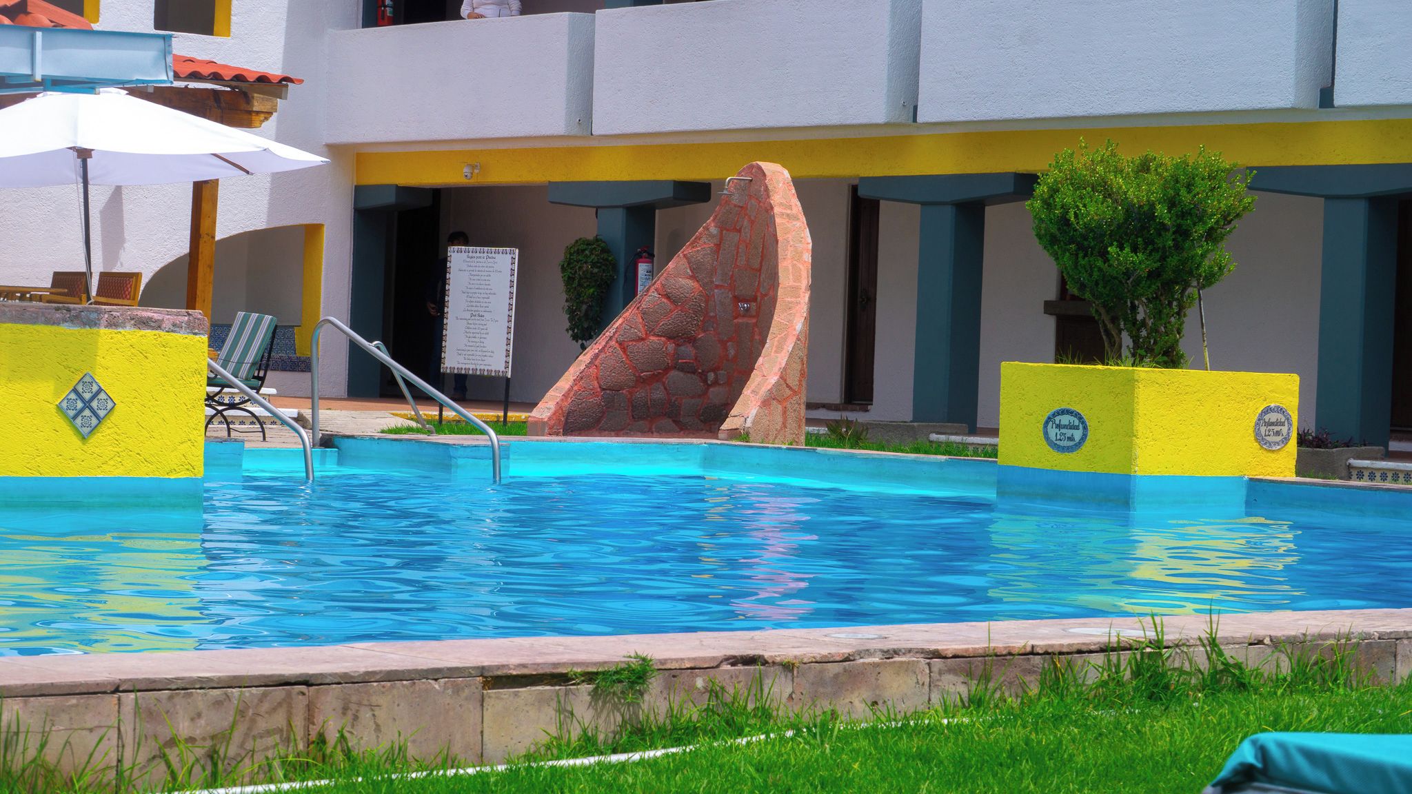 Una piscina con una escultura de piedra, una tumbona y un cartel.