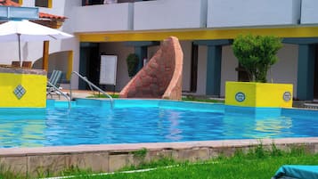 Una piscina con una escultura de piedra, una tumbona y un cartel.