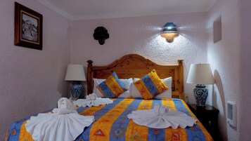 Habitación de hotel con una cama de madera, dos lámparas de noche, un aplique en la pared y un cuadro enmarcado.