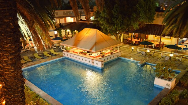 A pool area with a covered seating area, lounge chairs, and umbrellas. - Villas Arqueologicas Teotihuacan (Teotihuacan)