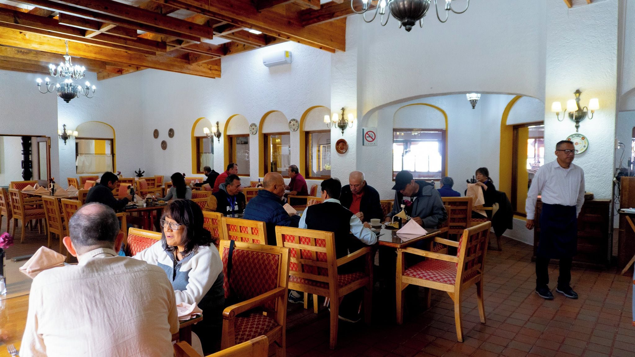 Un restaurant avec des meubles en bois, des lustres et un serveur.