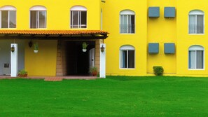 A yellow building with a tiled roof, multiple windows, and a well-maintained lawn. - Villas Arqueologicas Teotihuacan (Teotihuacan)