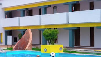 A hotel with a swimming pool, a rock feature, and a planter with a soccer ball.