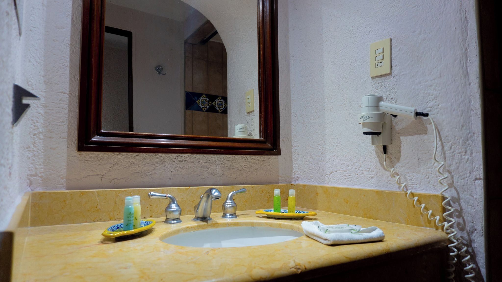 A bathroom with a sink, two faucets, a mirror, and a hairdryer on the wall.