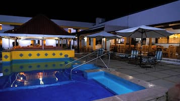 Una piscina con solárium enlosado, zona de estar al aire libre y sombrillas.