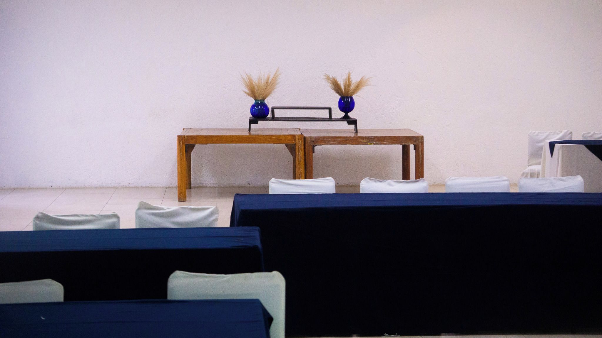 Une pièce avec une table en bois, deux vases bleus contenant des plantes séchées et des chaises blanches.
