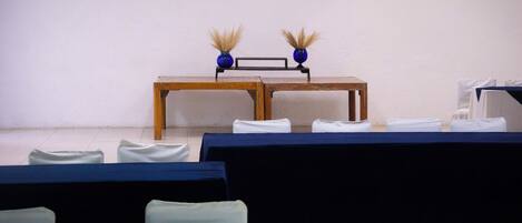 Une pièce avec une table en bois, deux vases bleus contenant des plantes séchées et des chaises blanches.
