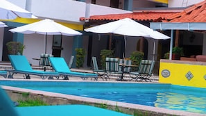 A pool area with lounge chairs and umbrellas, a tiled pool edge, and a building with a yellow wall and tiled roof. - Villas Arqueologicas Teotihuacan (Teotihuacan)
