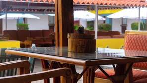A glass-top table with a wooden bowl and pine cone centerpiece, surrounded by wicker chairs and red patterned cushions. - Villas Arqueologicas Teotihuacan (Teotihuacan)