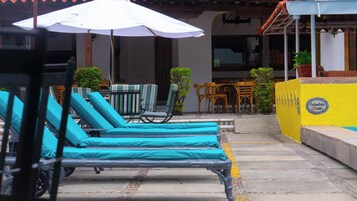 Outdoor lounge chairs with umbrellas, a yellow wall with a plaque, and a staircase leading to a building.