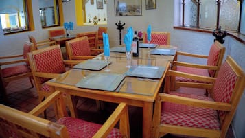Un comedor con mesas y sillas de madera, cada conjunto con un mantel individual, una copa de vino y una botella.