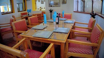 Un comedor con mesas y sillas de madera, cada conjunto con un mantel individual, una copa de vino y una botella.
