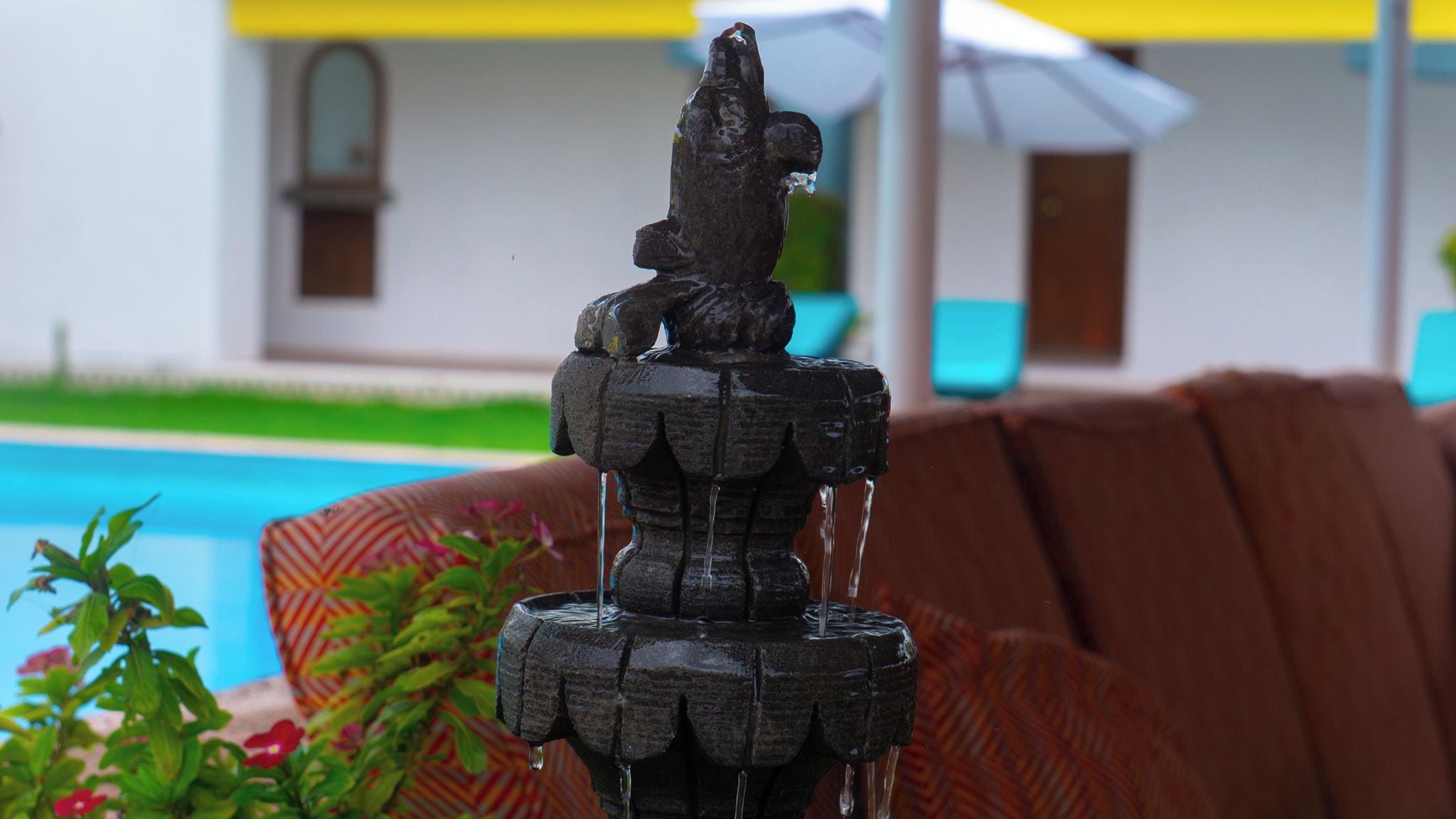 A stone fountain with water flowing, surrounded by greenery and a pool.