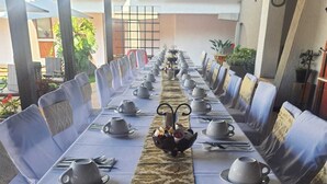 Una larga mesa de comedor preparada para una comida, con sillas a ambos lados, un camino de mesa estampado en el centro y una decoración ornamental.