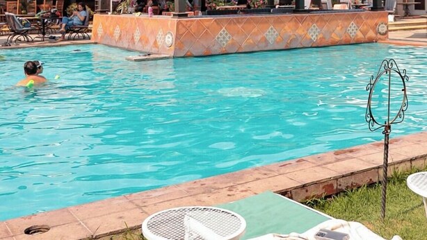 Una piscina con zona cubierta, sillas de descanso y una pequeña mesa.