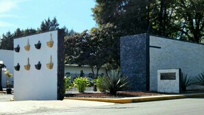 Un edificio moderno con fachada blanca y un muro azul decorativo, rodeado de jardines ajardinados y árboles.