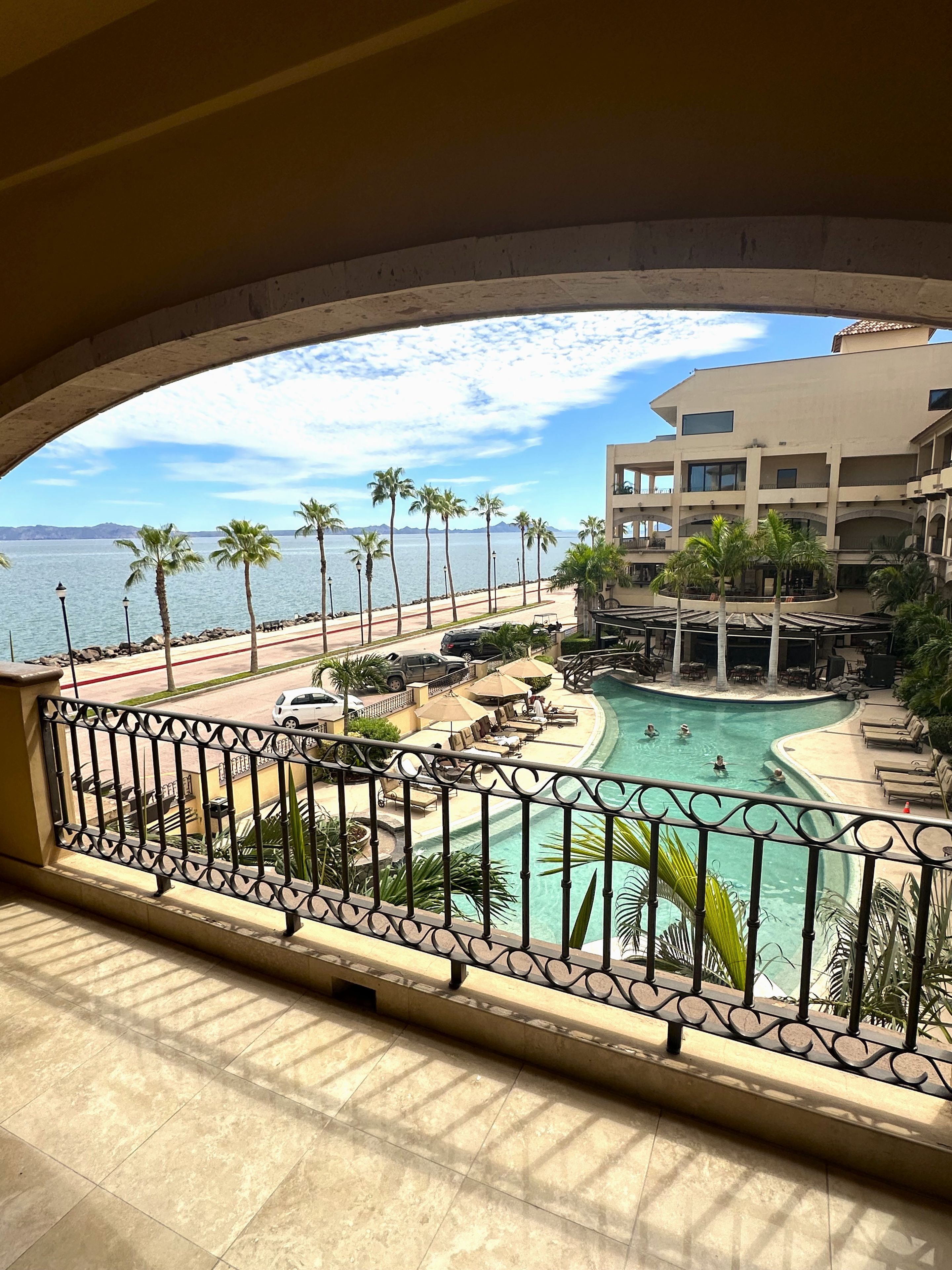 Vista de uma piscina com área de lazer, uma praia e um edifício com várias varandas.