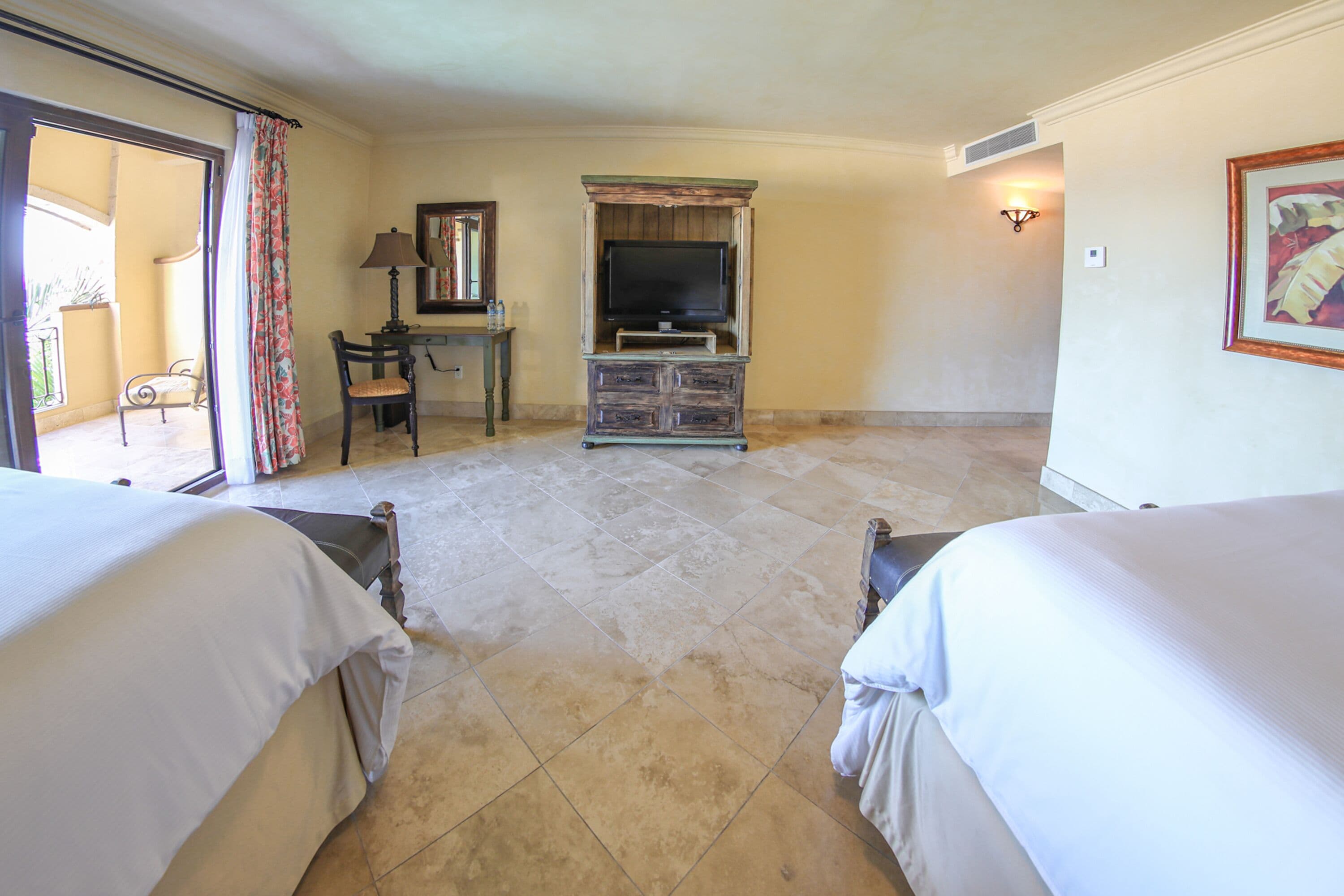 A hotel room with two beds, a television, a desk, and a chair.