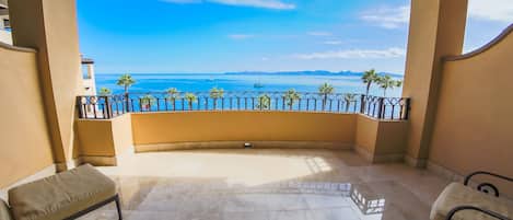 A balcony with a view of the sea, a bench, and a railing.