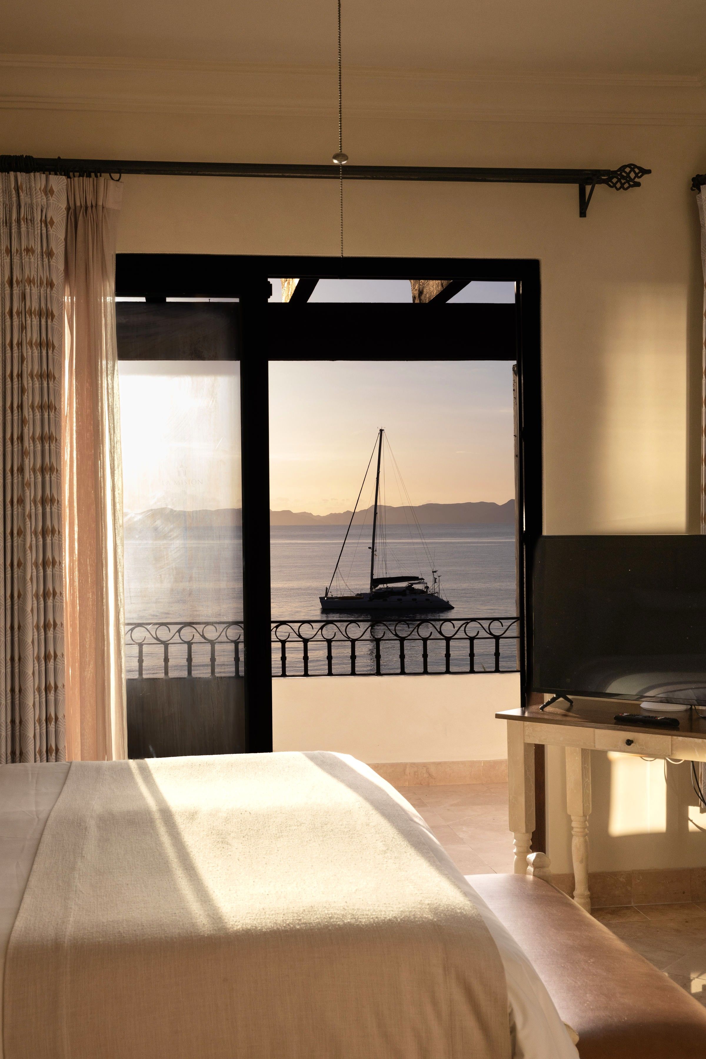 A bedroom with a bed, a desk, and a view of the sea through an open door.