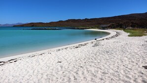 Una playa con agua turquesa cristalina, arena blanca y una pequeña estructura en la orilla.