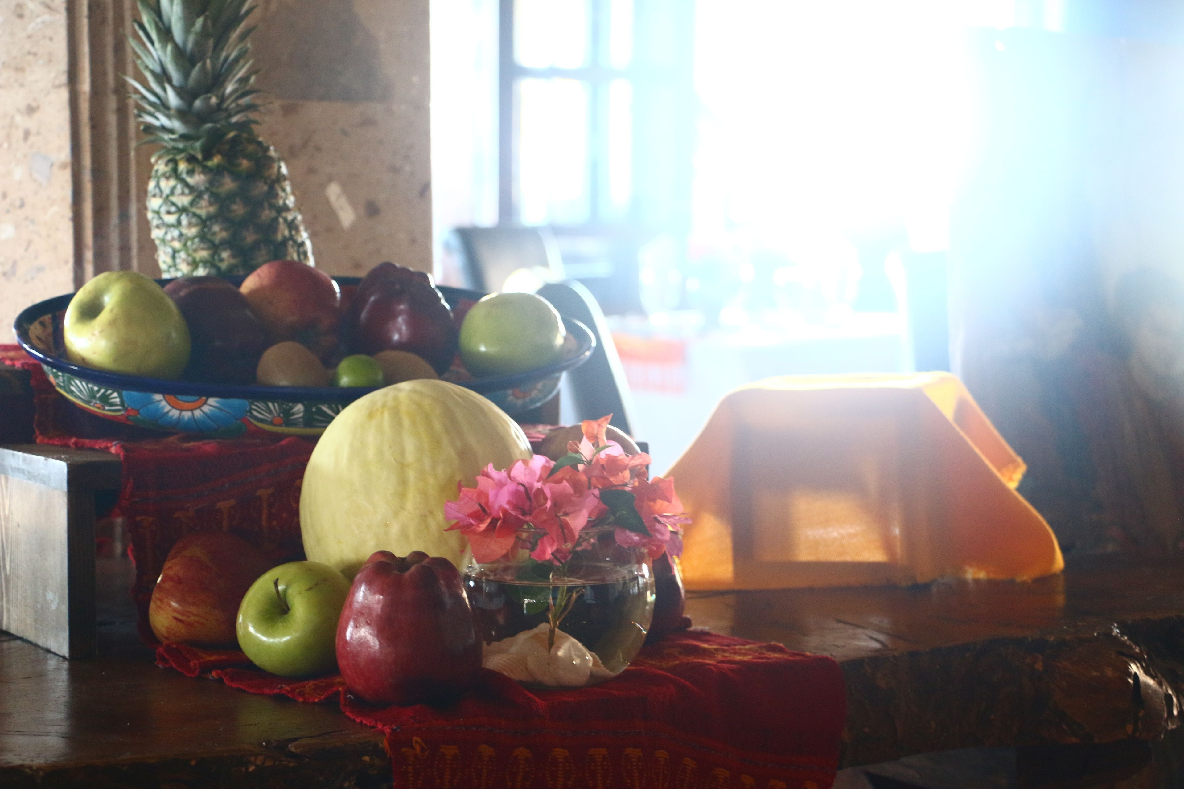 Ein Tisch mit einer Schale Obst, einer Ananas und einer Vase mit Blumen.