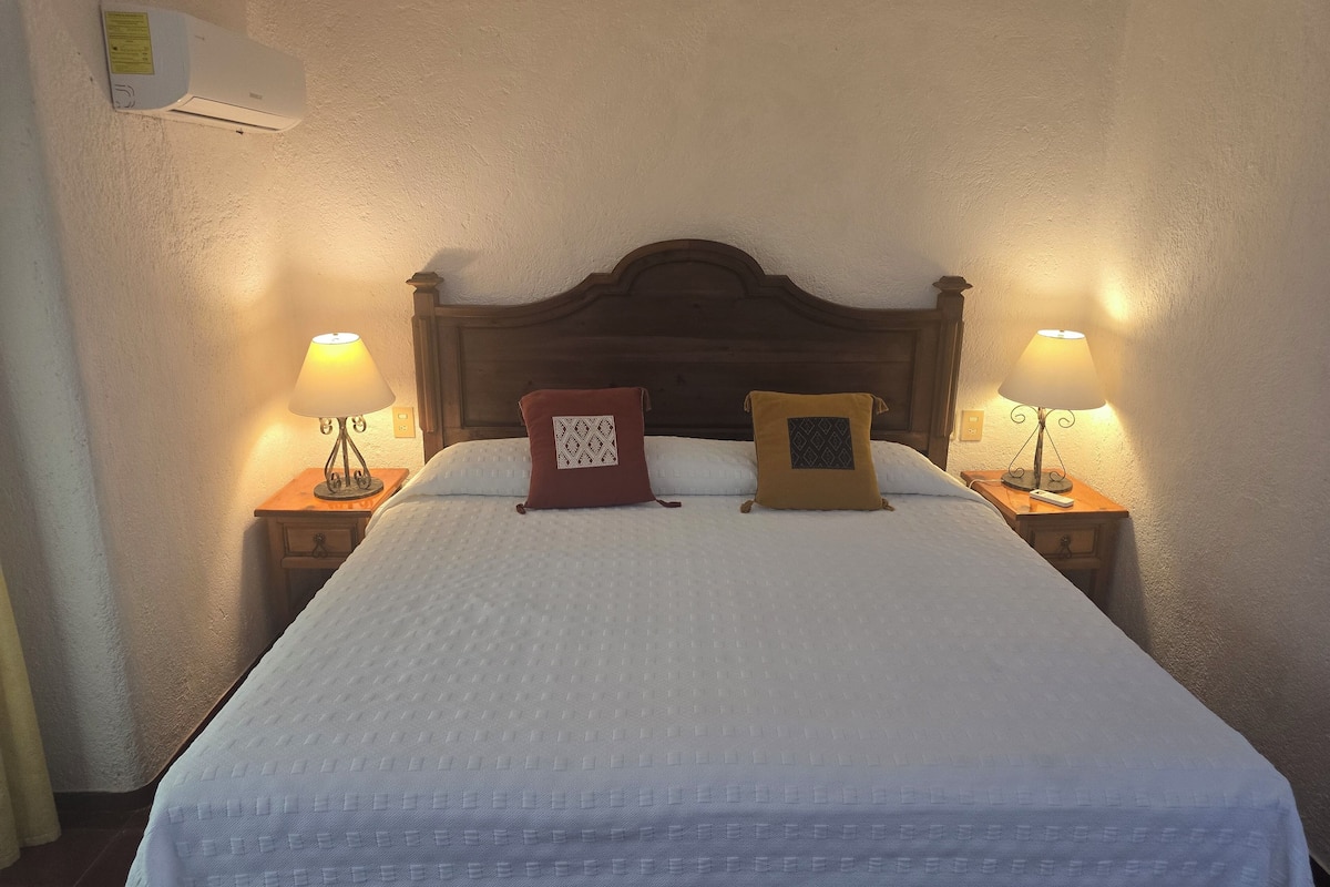 A neatly made bed with two pillows, a wooden headboard, and bedside lamps on either side.