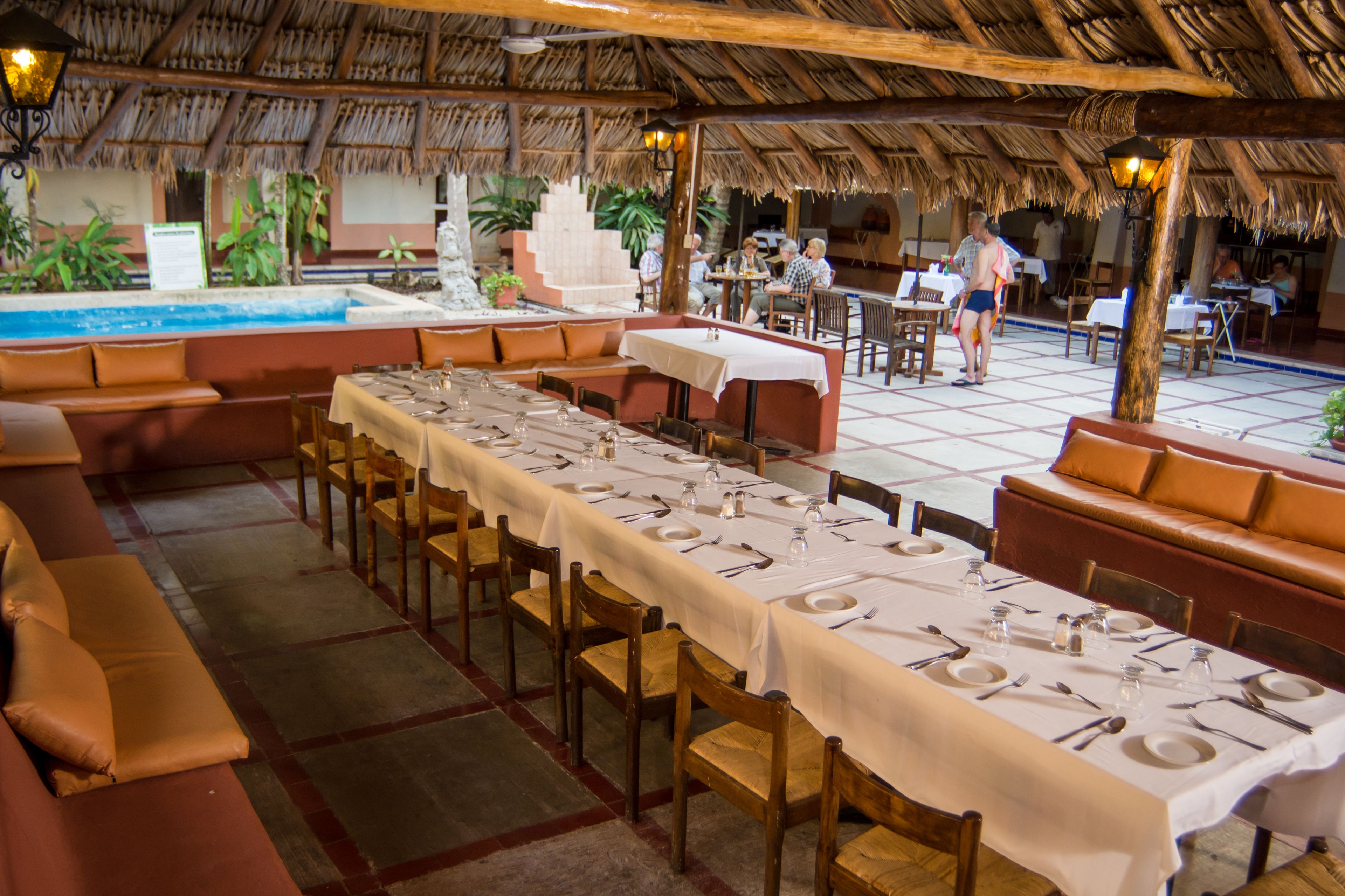 Un restaurante con mesas largas preparadas para comer, una zona de piscina y asientos al aire libre.