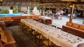 Un restaurante con mesas largas preparadas para comer, una zona de piscina y asientos al aire libre.