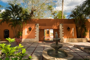 Un patio con una fuente, palmeras y la entrada a un edificio.