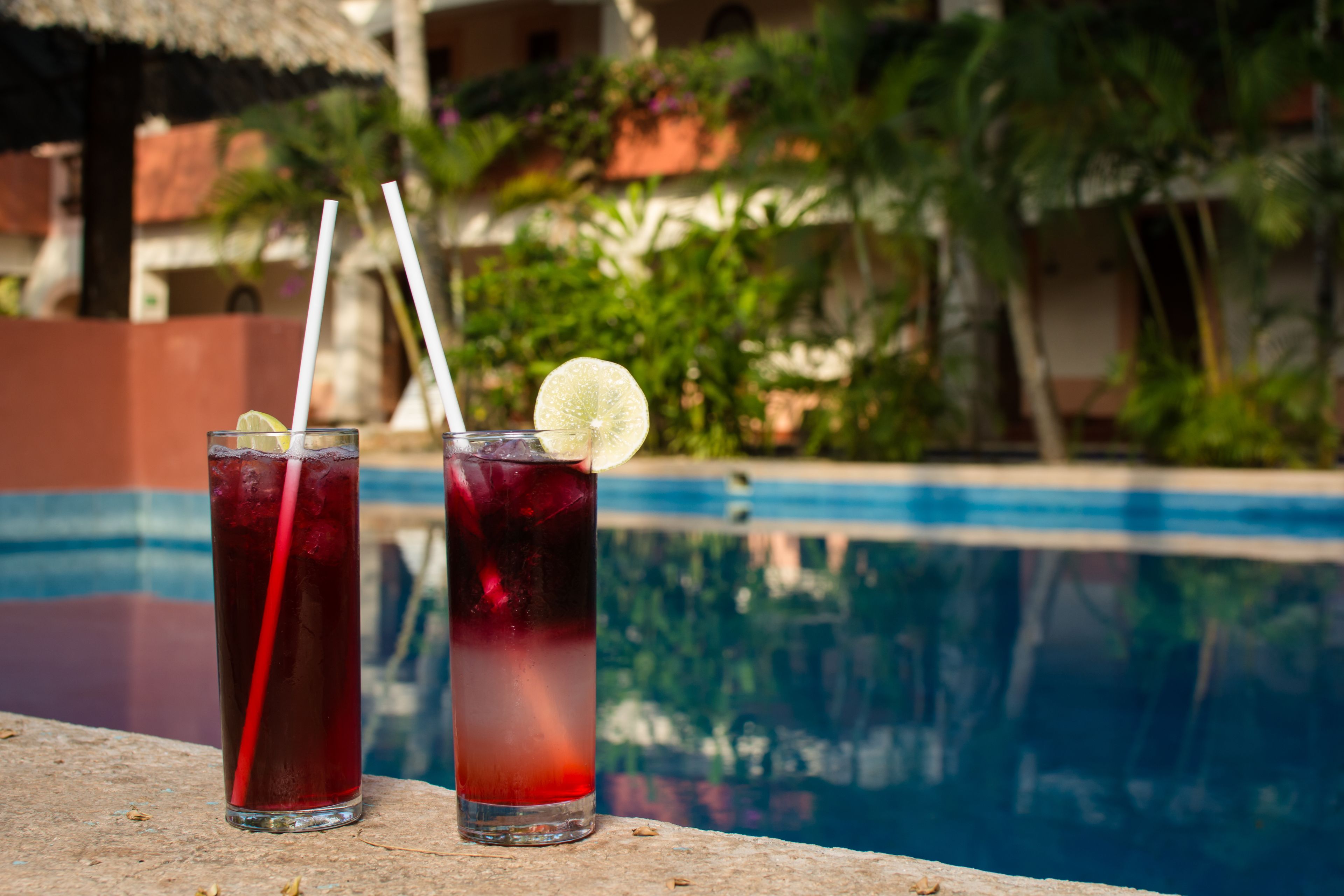 Dos vasos de bebida roja con pajitas y una rodaja de lima sobre una mesa junto a la piscina.